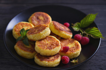 Cottage cheese pancakes on black plate. Syrniki and raspberries