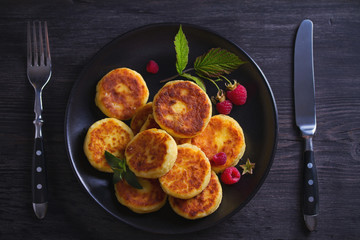Cottage cheese pancakes on black plate. Syrniki and raspberries