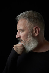Portrait of a brutal gray haired man with a gray lush beard and strict face on a black background, selective focus