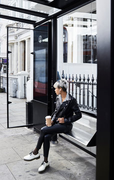 Female waiting at bus station with coffee.