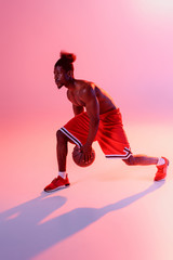 Fototapeta na wymiar shirtless african american sportsman with muscular torso playing basketball on pink background with gradient and lighting