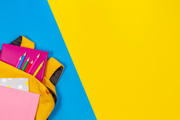 Back to school concept. Yellow backpack with school supplies on yellow and light blue background. Top view