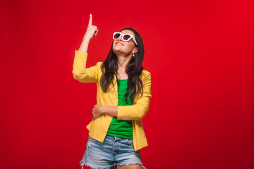 Fototapeta na wymiar Girl on red background in yellow jacket shows fingers up copy space