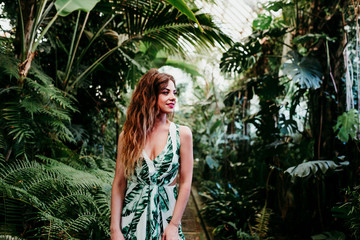 portrait of beautiful blonde young woman smiling at sunset in a green house surrounded by tropical plants. Happiness and lifestyle concept