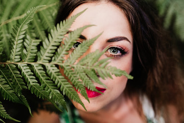 close up portrait of a young beautiful woman among green fern leaves looking at the camera. Beauty concept © Eva