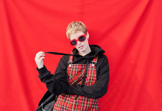 Fashionista holding strip of her hoodie on red wall.