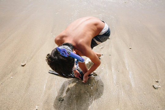 Boy putting on his fins on the sand with snorkel mask on
