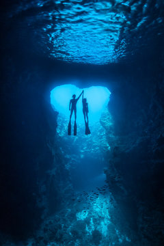 Couple free divers holding hands in the heart shape cavern with back light