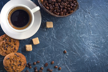 A cup of coffee with pieces of cane sugar, biscuits with chocolate and a vase with coffee beans. Top view