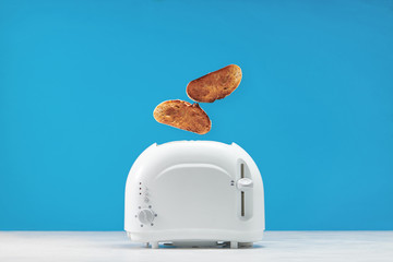 Roasted toast bread popping up of toaster with blue wall