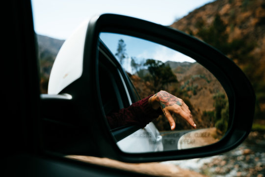 hand with tattoo seen from the rear-view mirror