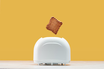 Roasted toast bread popping up of toaster with yellow wall - obrazy, fototapety, plakaty