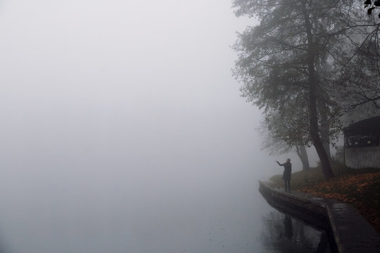 Woman standing on river bank in foggy autumn morning