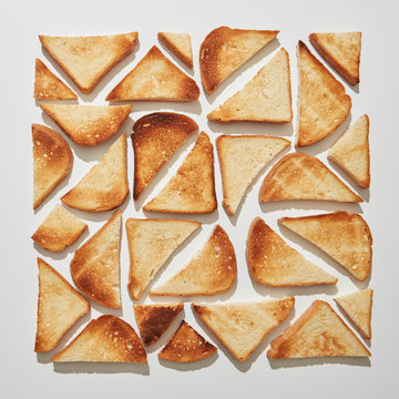 Pattern in the form of a square from different pieces of fried toast on a gray background with reflection of shadows. Food background. Flat lay
