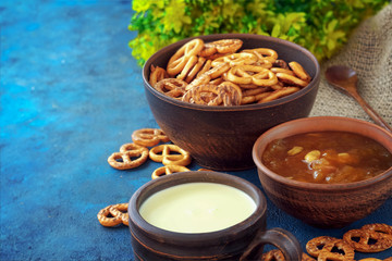 Still life in a rustic style. Crumbled pretzels on a textural background with milk in a clay cup, with apricot jam in a clay plate.
