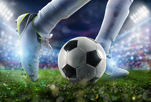 Football scene at night match with close up of a soccer shoe hitting the ball with power.