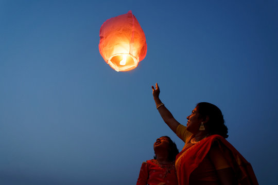 Little girl and her mother releasing sky lantern to the sky at twilight