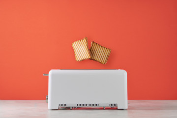 Roasted toast bread popping up of toaster with orange wall