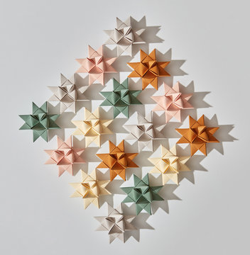 Different paper origami stars in shape rhombus on a gray background with reflection of shadows and copy space. Handcraft pattern. Flat lay