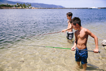 Two boys fishing for minnows in the ocean along the coastline of Hawaii