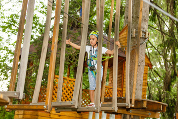 Fototapeta premium Adorable little girl enjoying her time in climbing adventure park on warm and sunny summer day. Summer activities for young kids. Child having fun on school vacations.
