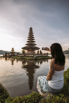 beautiful young woman taking a picture with her mobile phone from ulun danu beratan temple