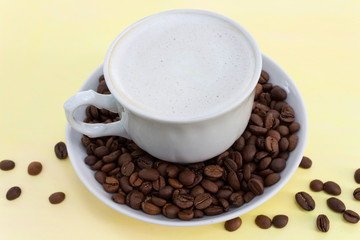 Cup of cappuccino coffee with milk froth and coffee beans on a yellow table, closeup. The concept of a soft and gentle summer cappuccino in yellow tones.