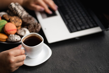 Unhealthy snack at work time. Woman eating cookies and drinking coffee at workplace. High calorie, fattening junk food, weight gain