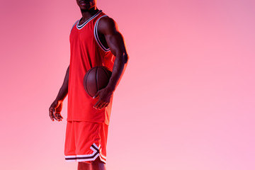 cropped view of african american basketball player holding ball on pink background with gradient © LIGHTFIELD STUDIOS