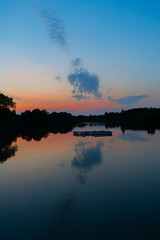 tranquil, twilight sunset shot over lake with reflections of sky and clouds in water and rowing boats to centre of lake