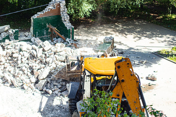 yellow excavator breaks a brick building in the yard