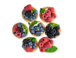 Tartlet with berries of raspberry, bilberry, blackberry, blueberry isolated on white background. Cake with berries, mint leaf and cheese cream. View from above