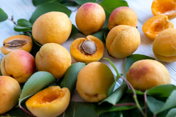 Ripe apricot fruit with green leaves close-up on a light wooden background. Summer fruit containing pectin.