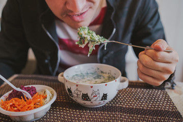 Cold soup with fresh cucumbers, radishes, potato and sausage with yoghurt in bowl. Salads from fresh vegetables: cabbage, carrots, beets in a white plastic plate.