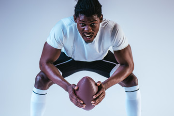 excited african american sportsman screaming while playing american football on blue background