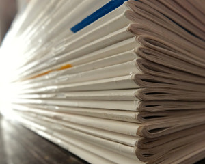 Stack of papers, white-sheet magazines focused on edge with light and blur.