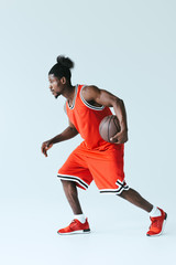 Fototapeta na wymiar african american sportsman in red sportswear playing basketball on grey background