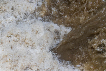 Fototapeta na wymiar Brown and white water mix in raging river after heavy rain
