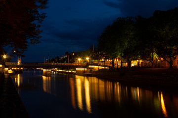 Fototapeta premium Night view of the historic bridge over the Auraioki River with a reflection in the water against the backdrop of a summer, dark, night cityscape. Turku city, Finnish landmark.