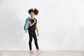 Fototapeta na wymiar Stylish African-American girl in jeans near white brick wall