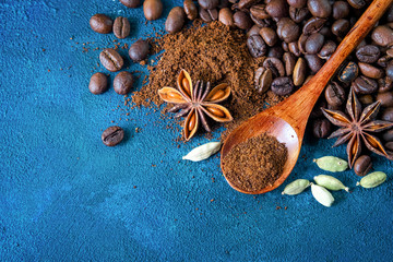 Flat lay. Coffee grains scattered on a blue textural background, anise stars, cardamom and ground coffee in a wooden spoon. Top view. Food concept.