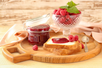 Tasty raspberry jam with fresh bread on wooden board