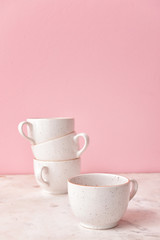 Ceramic cups on light table against color background