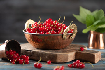 Red currant in a metal bowl on wooden background