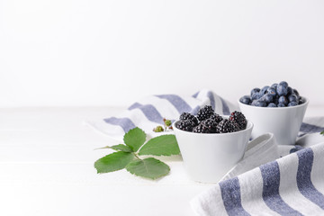 Fototapeta na wymiar Bowls with tasty blackberries and blueberries on white table