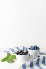 Bowls with tasty blackberries and blueberries on white table