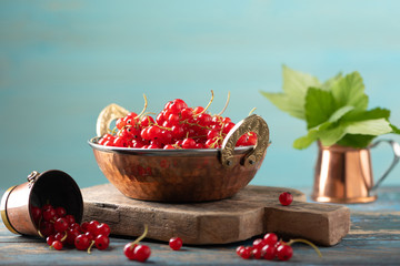 Red currant in a metal bowl on wooden background