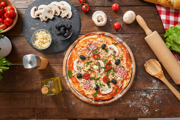 Homemade Pizza on wooden board, with tomatoes and salami, mushrooms, Italian style on old wooden table, top view.