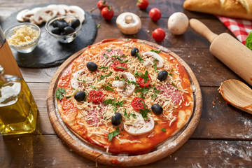 Homemade Pizza on wooden board, with tomatoes and salami, mushrooms, Italian style on old wooden table, top view.