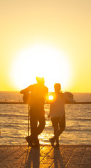unfocused vertical wallpaper photography of couple human silhouette back to camera enjoy by beautiful orange sunset above Mediterranean sea background from view point observation deck, copy space 